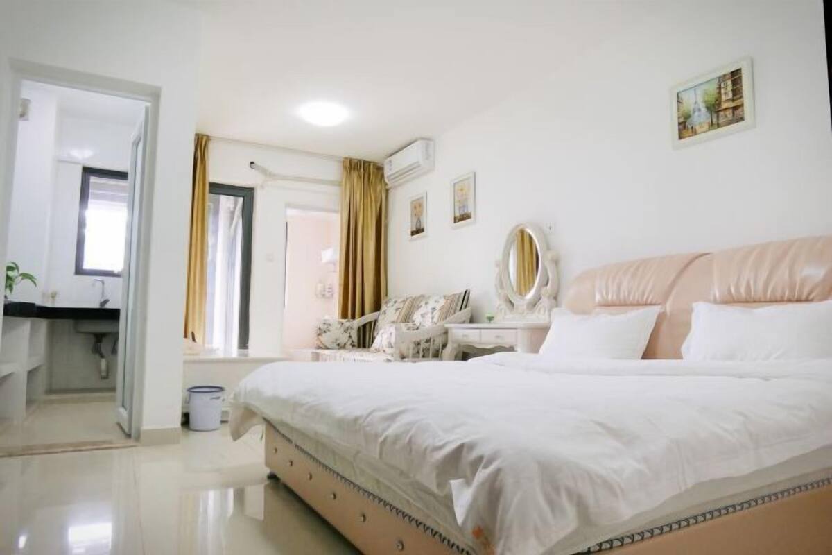 A bedroom with a large bed, a bedside table, a mirror, and a window with curtains.