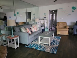A living room with a grey sofa, a coffee table, and a patterned rug. There is a door leading to another room. - Rest & recharge, close to the beach! Spacious condo for a beach getaway! (Little River)