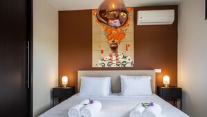 Une chambre d’hôtel avec un grand lit, deux tables de chevet avec des lampes, un climatiseur fixé au mur et un tableau décoratif au-dessus du lit.