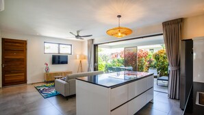 Une cuisine moderne dotée d’un îlot central, d’un coin repas avec des chaises, d’un ventilateur de plafond et d’une grande fenêtre avec des rideaux.