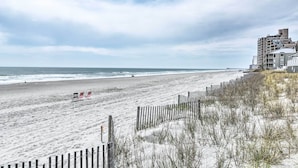 A beach with a wooden fence, beach chairs, and a building in the background. - Resort Home ~ 1 Mi to Myrtle Beach Access! (Myrtle Beach)