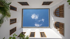 A room with a large skylight, multiple windows with decorative grills, and a view of the sky. - Riad Rossi (Marrakech)