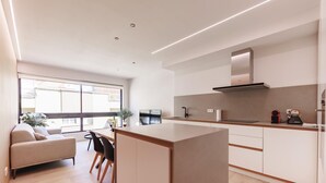 A modern kitchen with a central island, a dining area with a sofa and chairs, and a large window providing natural light. - Bravissimo Centre, Modern 2-bedroom apartment (Girona)