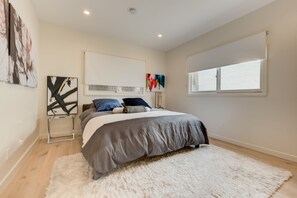 A bedroom with a bed, a white fluffy rug, a window, and abstract art on the walls.