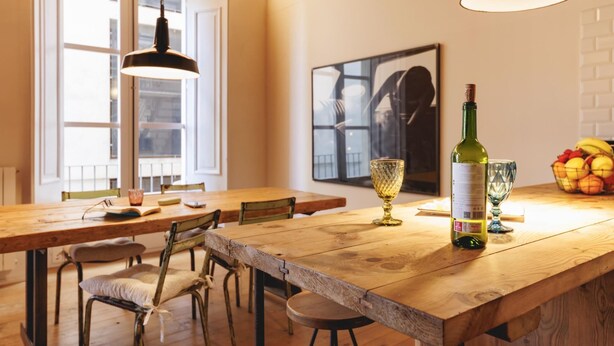 A kitchen with a wooden table, chairs, a hanging light fixture, a wine bottle, and a fruit basket. - Bravissimo Carrer Nou, cosy 2-bedroom apartment in the center of Girona (Girona)