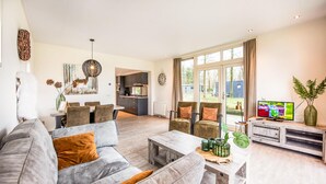 A modern living room with a grey sofa, a coffee table, and a TV. There's a dining area with a table and chairs, and a kitchen in the background. - 2 bedroom lovely home in Zorgvlied (Zorgvlied)