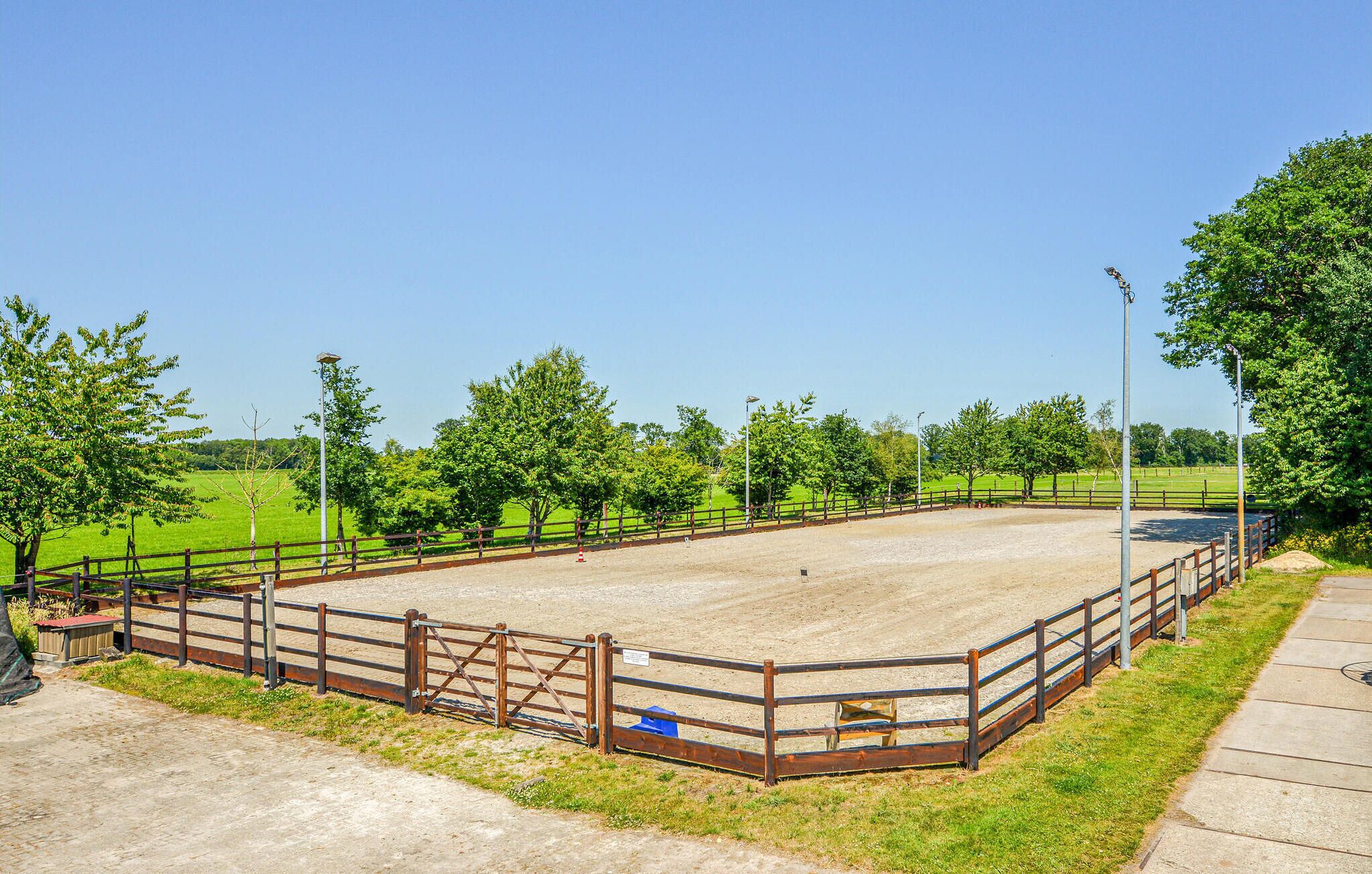 Una arena al aire libre con una pista de tierra, rodeada por una valla de madera, árboles y un cielo despejado.