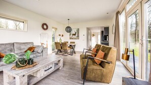 A spacious living room with a grey sofa, a wooden coffee table, and a brown armchair. There is a dining area with a table and chairs, and a kitchen in the background. - 2 bedroom lovely home in Zorgvlied (Zorgvlied)