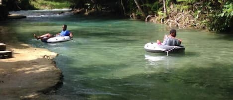 Two people floating on inflatable tubes in a clear river surrounded by greenery.