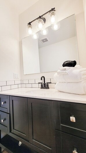 A bathroom with a white sink, black cabinets, a mirror with lights, and a stack of white towels.