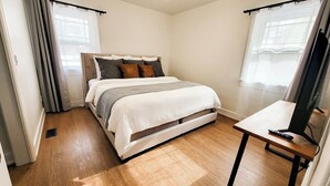 Um quarto com uma cama, mesa de cabeceira e televisão.
