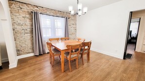 Uma sala de jantar com parede de tijolos, mesa e cadeiras de madeira e um candelabro.