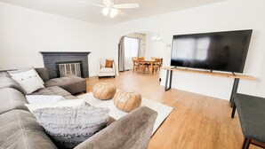 Uma sala de estar moderna com sofá, puf e uma TV de tela plana fixada na parede.