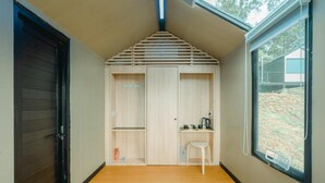 A compact room with a sloped ceiling, a small table with a chair, and a window with a view of the outdoors. - Bobocabin Gunung Mas (Cisarua)