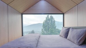 A bedroom with a large window, a bed, and a view of mountains. - Bobocabin Gunung Mas (Cisarua)