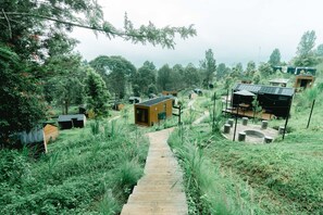 A forested area with a wooden pathway leading to several small cabins. - Bobocabin Gunung Mas (Cisarua)