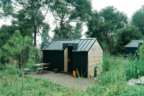 A small, rustic cabin with a sloped metal roof, surrounded by dense greenery. - Bobocabin Gunung Mas (Cisarua)