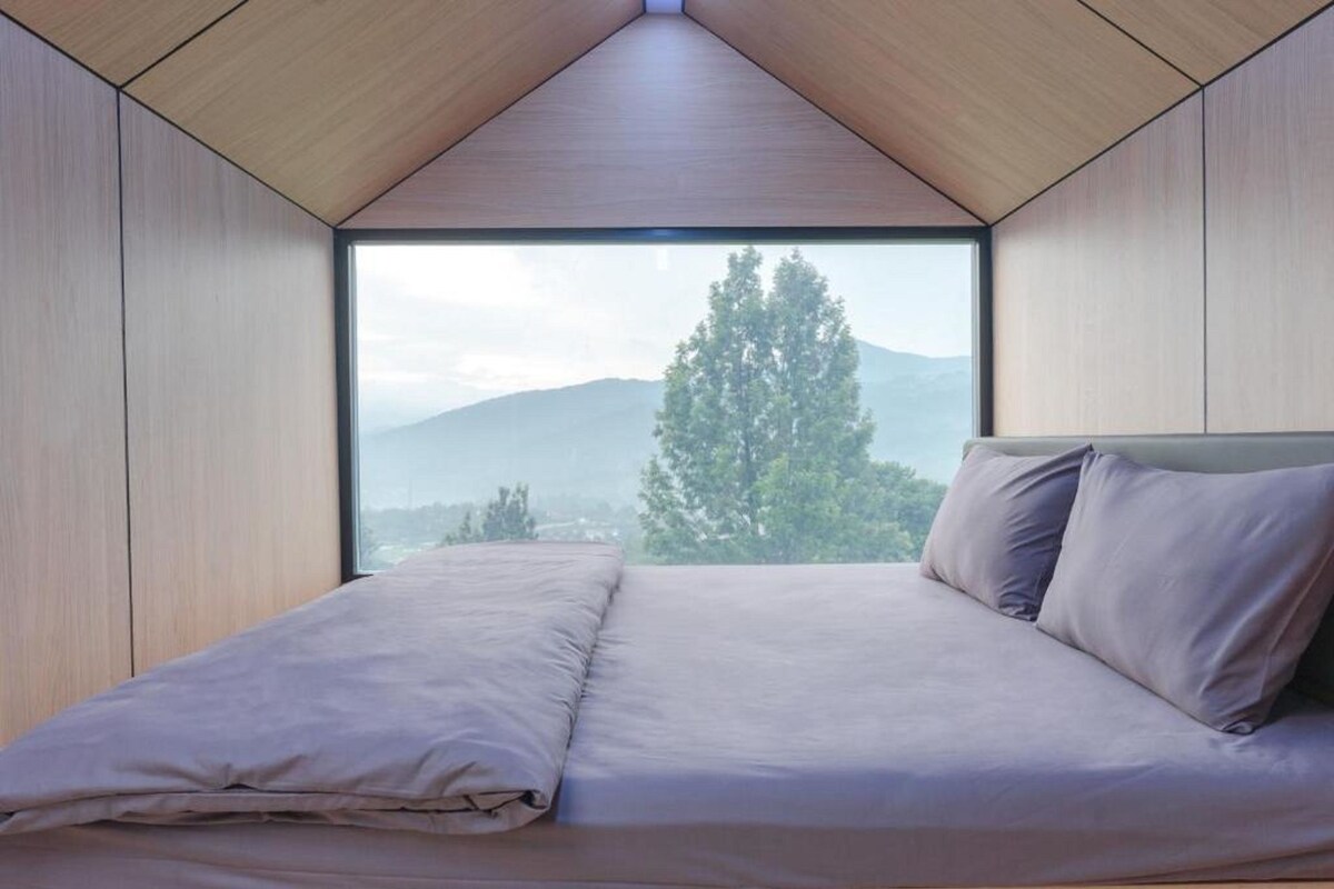 A bedroom with a large window, a bed, and a view of a mountain.