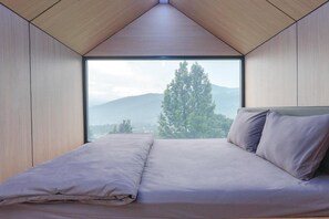 A bedroom with a large window, a bed, and a view of mountains. - Bobocabin Gunung Mas (Cisarua)