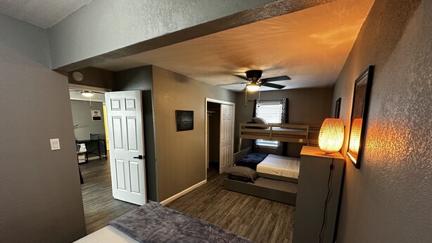A compact room with a bunk bed, a ceiling fan, and a wall-mounted lamp. - 2-Bedroom in the Heart of SA (San Antonio)