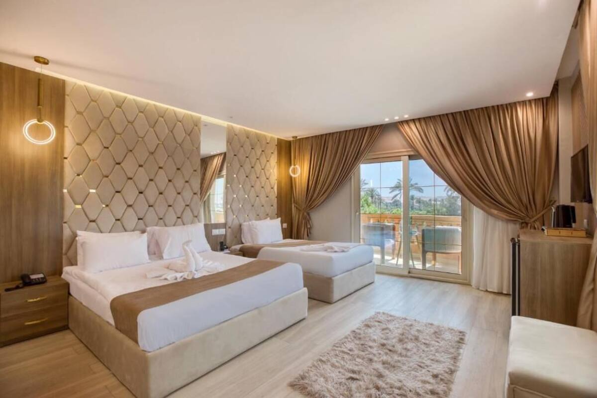 A modern hotel room with a large bed, two smaller beds, a sofa, a TV, and a balcony with curtains.