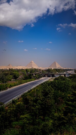 A highway with a bridge over a river, surrounded by greenery and three pyramids in the background.