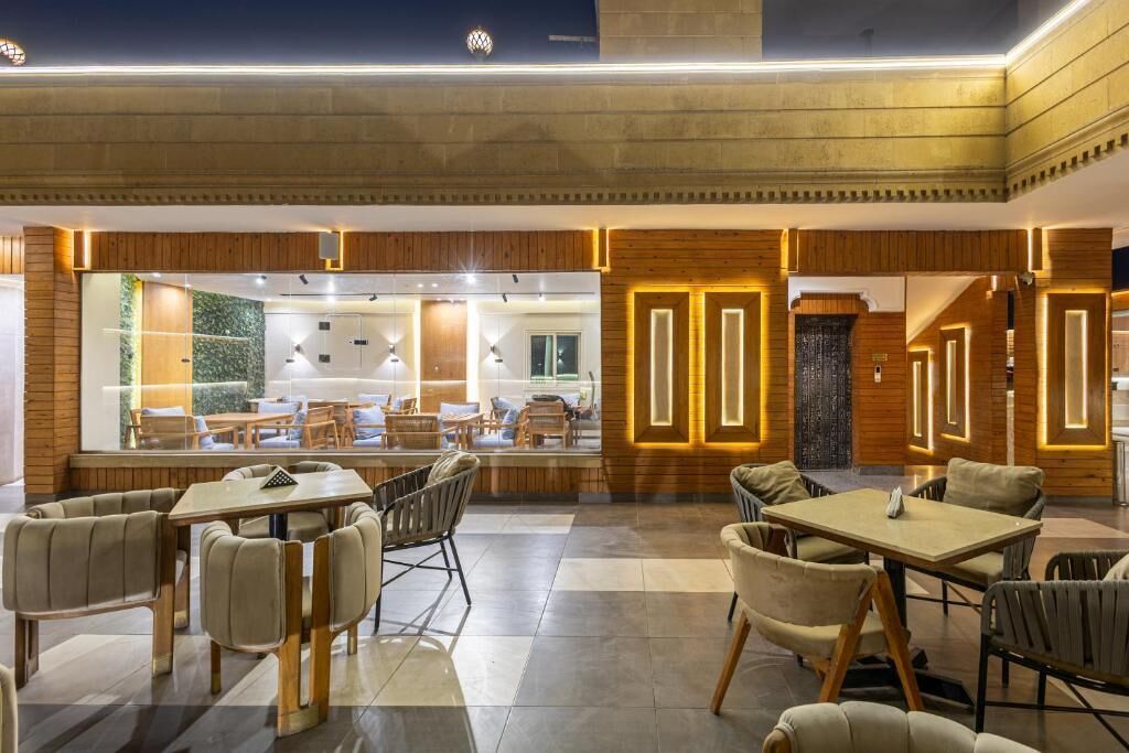 A modern interior with wooden paneling, a large seating area with tables and chairs, and a view through a glass wall.
