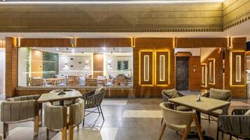 A modern interior with wooden paneling, a large seating area with tables and chairs, and a view through a glass wall.