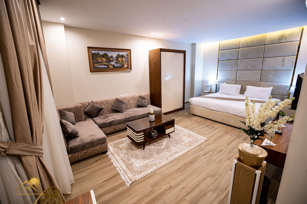 A modern hotel room with a sofa, a bed, a wooden coffee table, and a decorative plant.