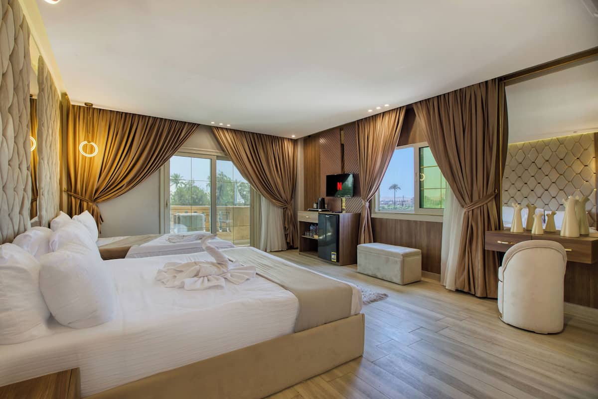 A modern hotel room with a large bed, a TV, a desk, and a view of the outdoors.