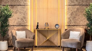 A lobby with two plush armchairs, a gold console table with decorative items, and a marble wall. - Pyramids Sunrise Inn (Giza)
