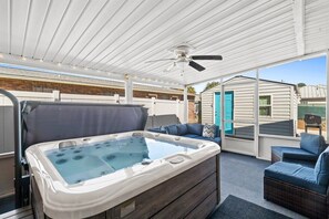 A covered outdoor area with a hot tub, seating, and a ceiling fan.