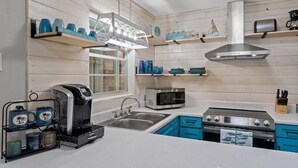 Een moderne keuken met witte aanrechtbladen, blauwe kastjes, een roestvrijstalen afzuigkap, een koffiezetapparaat, een magnetron en een spoelbak.