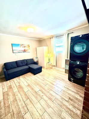 Un salon avec un canapé d’angle, un lave-linge et un tableau accroché au mur.