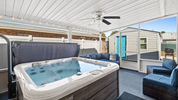 Een overdekt buitengebied met een jacuzzi, zitplaatsen en een plafondventilator.