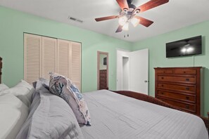 A bedroom with a bed, a dresser, a television, and a ceiling fan.