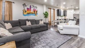 A modern living room with a grey sofa, a white sofa, and a dining area with a table and chairs. - NorthATX Urban Oasis Pool 5BR 2BA Game room Office (Pflugerville)