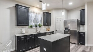 A modern kitchen with dark cabinets, a central island, stainless steel appliances, and pendant lighting. - NorthATX Urban Oasis Pool 5BR 2BA Game room Office (Pflugerville)