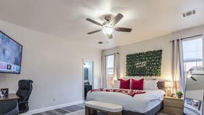 A bedroom with a bed, a desk, a chair, a bench, a ceiling fan, a mirror, and a wall with greenery. - NorthATX Urban Oasis Pool 5BR 2BA Game room Office (Pflugerville)