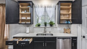 A kitchen with dark cabinets, a white countertop, a stainless steel sink, and a window with sheer curtains. - NorthATX Urban Oasis Pool 5BR 2BA Game room Office (Pflugerville)