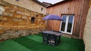 Un patio con una mesa y sillas, un paraguas morado y un muro de piedra.
