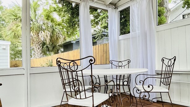A covered patio with a table and chairs, a glass table, and a view of greenery outside. - Historic Cozy Parkside Cottage in Savannah (Savannah)