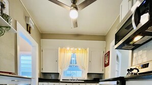 A kitchen with white cabinets, a black oven, and a ceiling fan. - Historic Cozy Parkside Cottage in Savannah (Savannah)