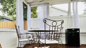A covered patio with a metal table and chairs, a woven rug, and a black refrigerator. - Historic Cozy Parkside Cottage in Savannah (Savannah)