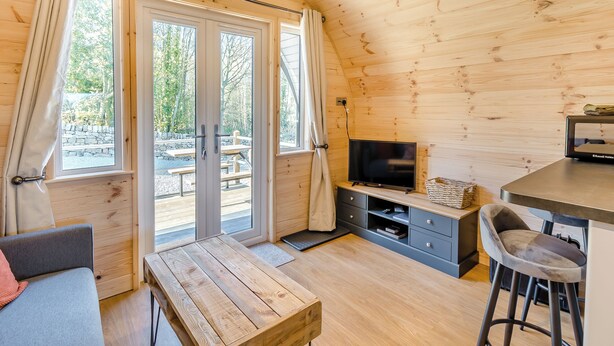 A cozy cabin interior with a wooden ceiling, a TV on a stand, a dining table, and a sofa. - Wood View - UK43707 (Scarborough)