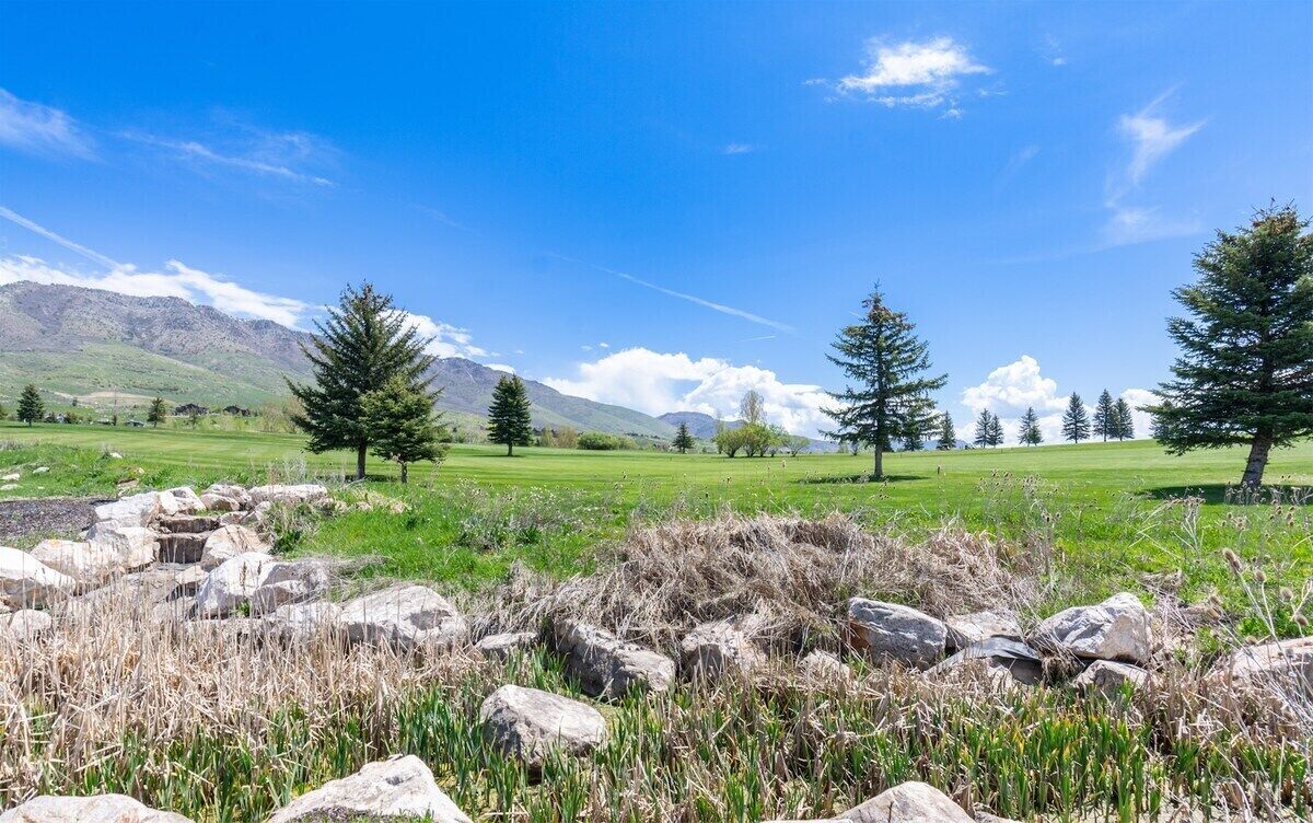 A mountainous landscape with a clear sky, green fields, and scattered trees.