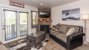 A living room with a stone fireplace, a leather sofa, a mounted TV, and a ski lift sign. - Adventure Awaits at Mountain Hollow Retreat in Eden! (Eden)