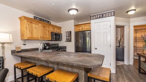 A kitchen with wooden cabinets, a stainless steel refrigerator, a bar stool area, and a 'Happy Hour' sign. - Adventure Awaits at Mountain Hollow Retreat in Eden! (Eden)
