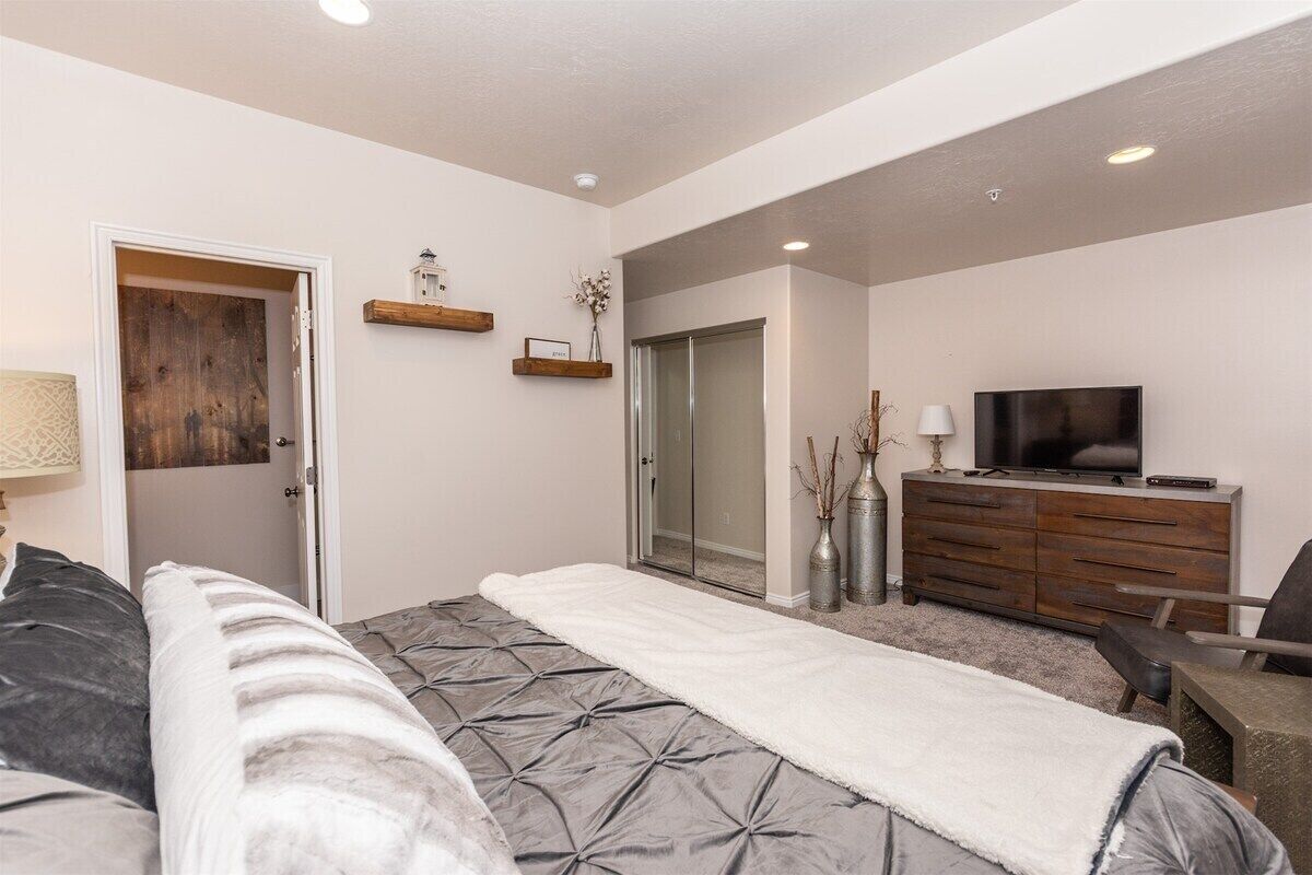 A bedroom with a bed, a dresser, a TV, and a door leading to another room.
