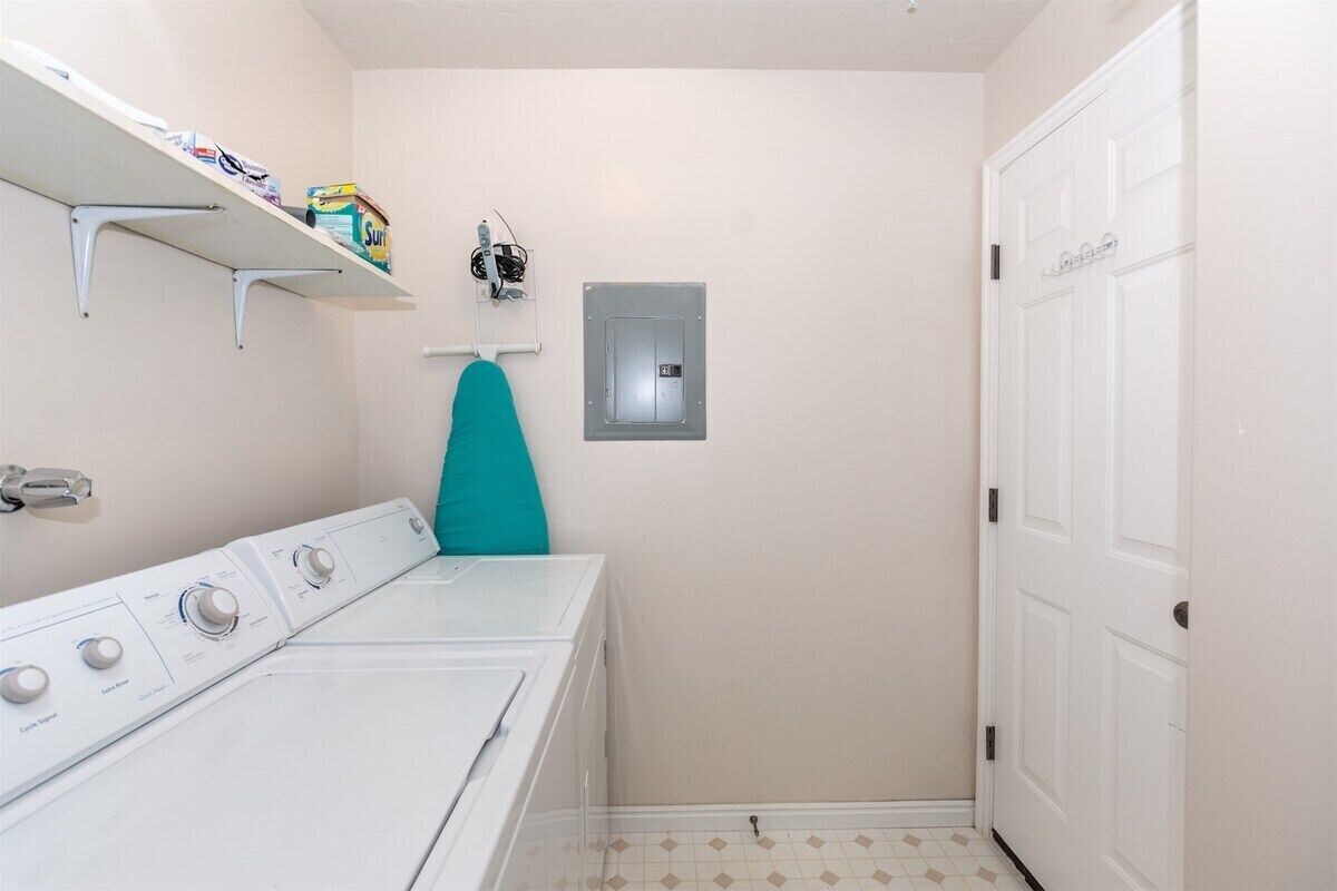 A laundry room with a washing machine, a drying rack, and a shelf with laundry supplies.